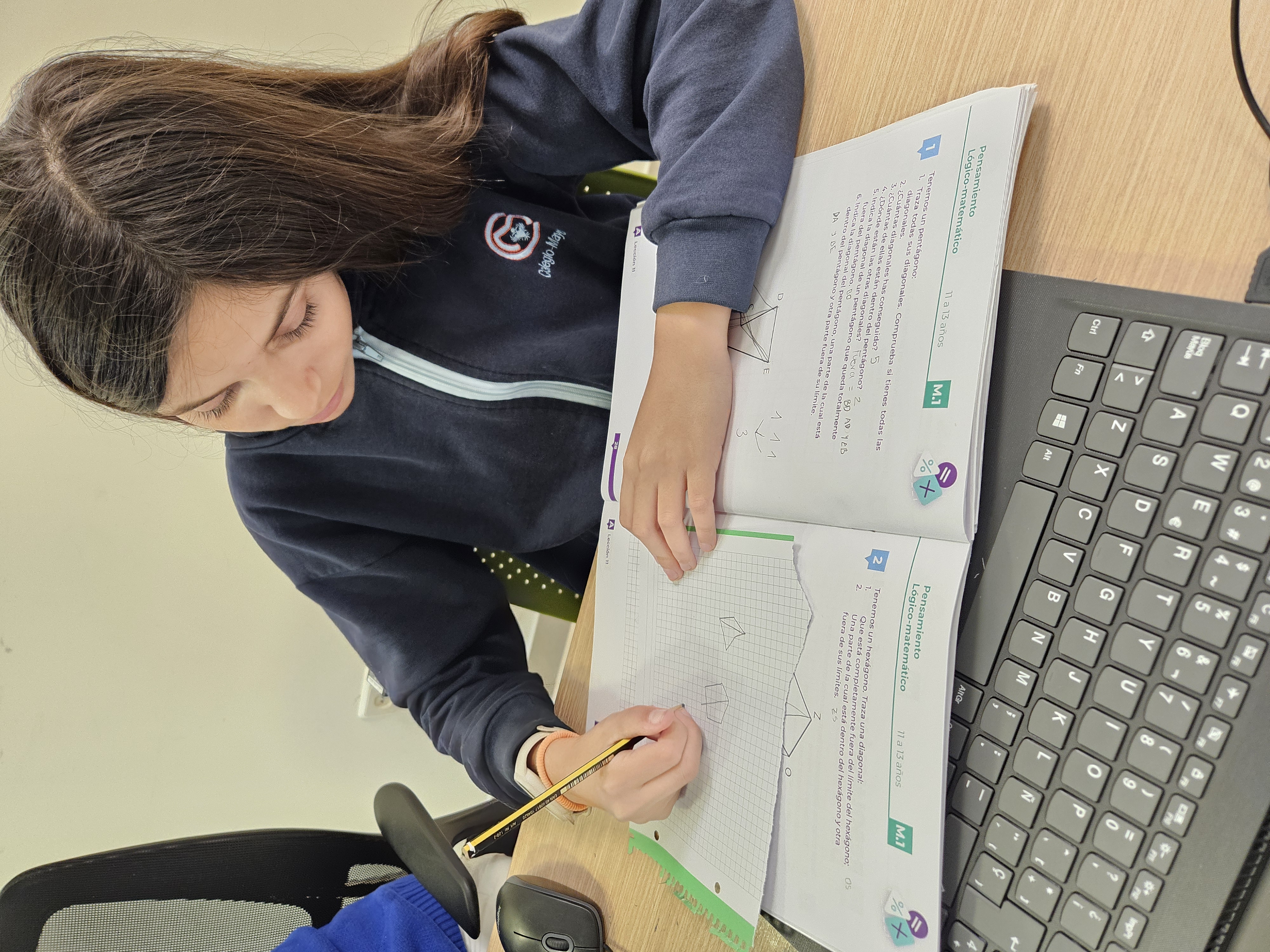 Alumna de Algorithmics resolviendo ejercicios de lógica matemática y pensamiento computacional sobre papel junto a un ordenador