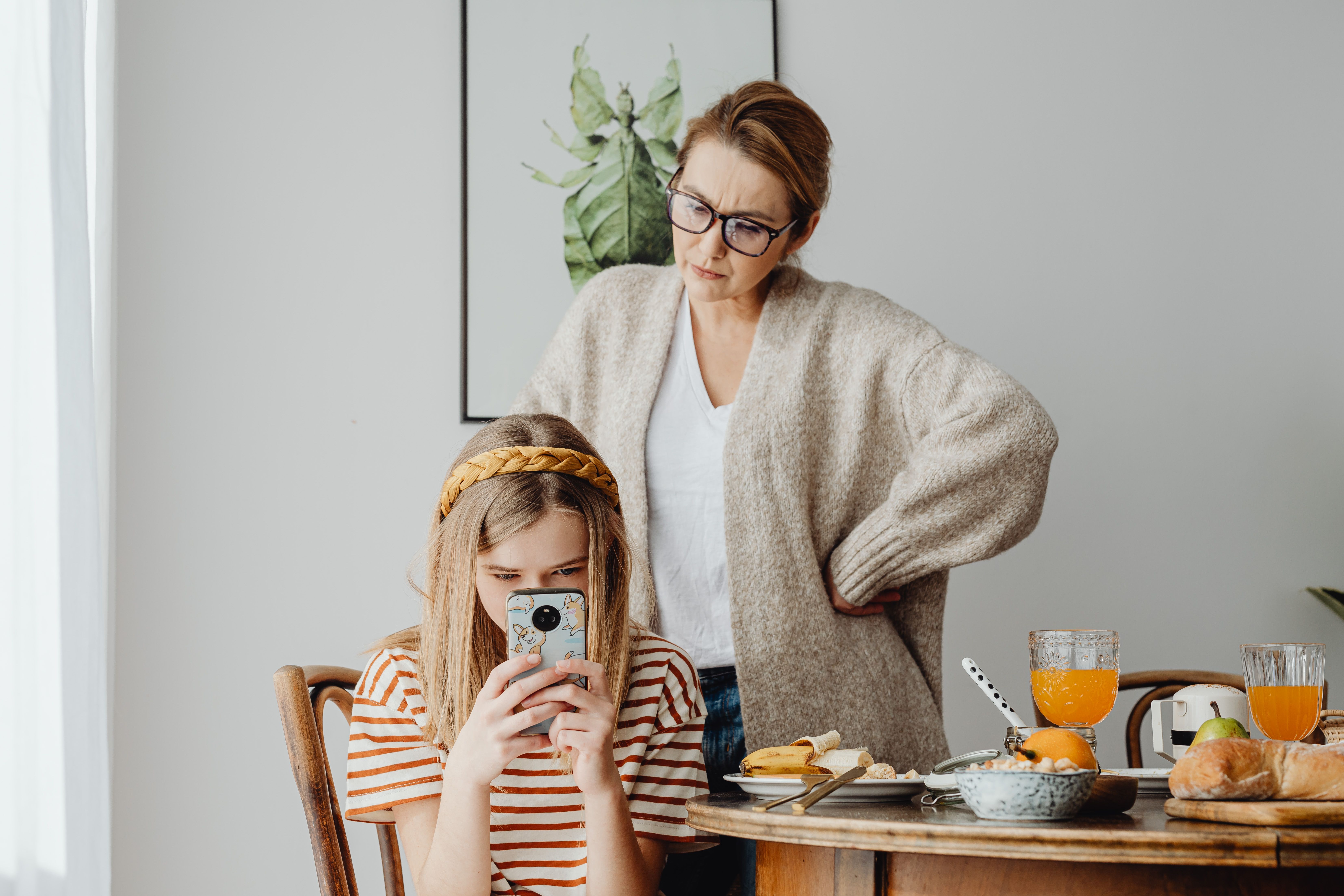 Madre observando a su hija mientras usa el móvil durante un momento familiar en casa